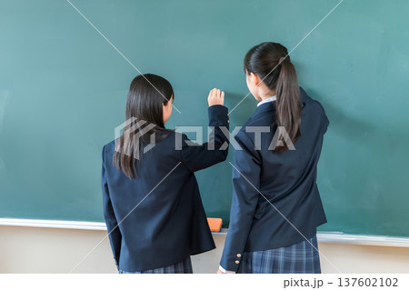 教室の黒板にチョークで文字を書く中学生の女子生徒 教室の黒板にチョークで文字を書く中学生の女子生徒 137602102
