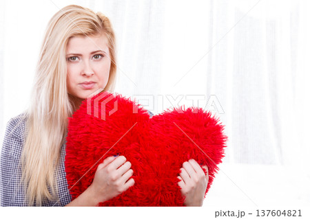 Sad woman holding red pillow in heart shape 137604821
