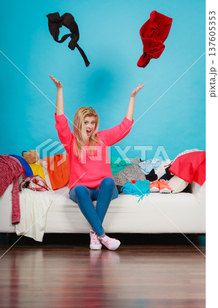 Woman sitting on messy couch throwing clothes 137605353
