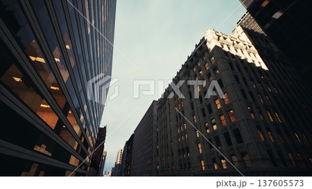 dusk between narrow skyscrapers with glowing. historic stone facades and glass towers frame sky, warm interior lights visible through grid of windows, cinematic dusk between narrow skyscrapers with glowing. historic stone facades and glass towers frame sky, warm interior lights visible through grid of windows, cinematic 137605573