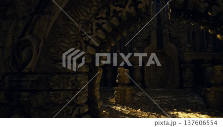 Closeup of carved arch leading toward dimly lit chamber with scattered coins and ornate reliefs, intimate texture study with cinematic lowkey lighting. 137606554