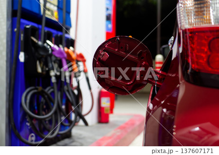 Modern Gas Station Service, An open red car fuel door sits in the foreground at a gas station, with colorful pump nozzles blurred in the background. Modern Gas Station Service, An open red car fuel door sits in the foreground at a gas station, with colorful pump nozzles blurred in the background. 137607171