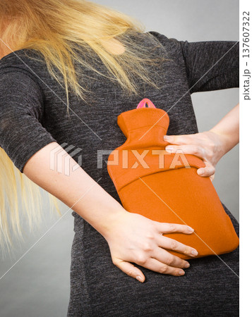 Girl having back pain, holding hot water bottle 137607322