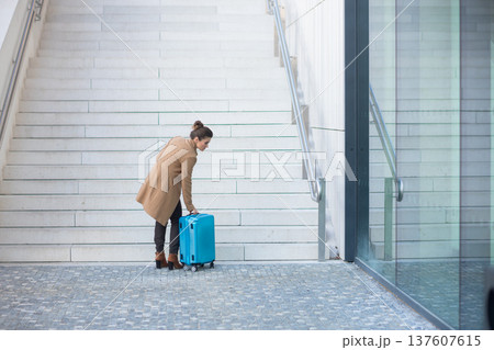 Woman Adjusting Suitcase at Train Station Stairs 137607615