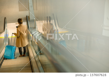 Woman Using Smartphone on Escalator with Suitcase 137607628