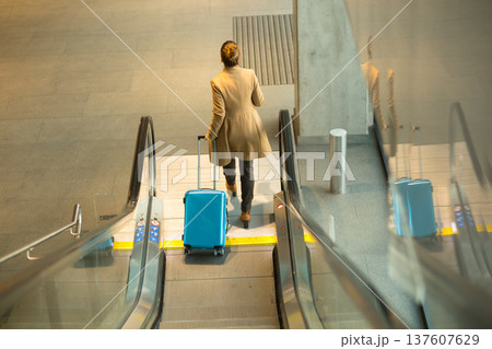Woman with Blue Suitcase Ascending Modern Escalator 137607629