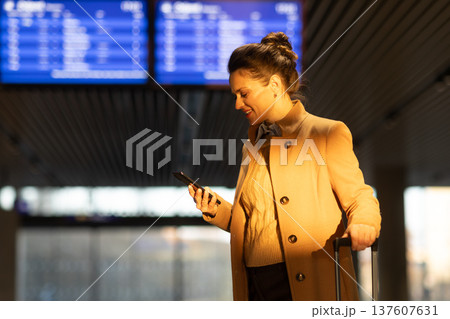 Smiling Woman Checking Train Schedule on Smartphone at Station Smiling Woman Checking Train Schedule on Smartphone at Station 137607631