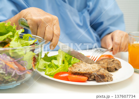 Asian elderly woman patient eating pork chop stake and vegetable salad for healthy food in hospital. Asian elderly woman patient eating pork chop stake and vegetable salad for healthy food in hospital. 137607734