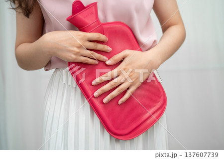 Woman using hot water bottle to relieve menstrual abdominal pain. Woman using hot water bottle to relieve menstrual abdominal pain. 137607739