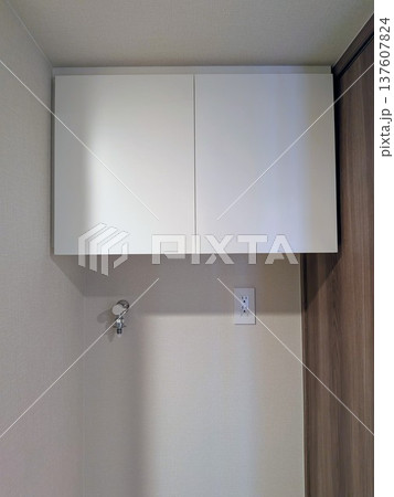 マンションの洗濯機置き場に設置された白のランドリー吊り戸棚と水栓・コンセント 137607824