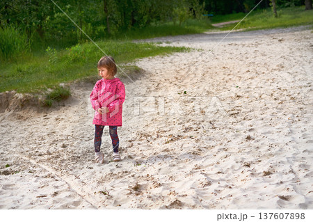 Little girl in red jacket playing on sand on nature 137607898