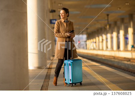 Woman with Suitcase Checking Phone at Train Station 137608025