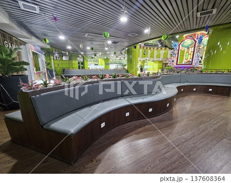 A modern waiting lounge featuring curved grey cushioned benches with integrated power outlets, decorated with festive green hanging ornaments and potted plants under a contemporary slatted ceiling. 137608364
