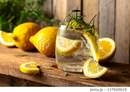 Summer refreshing drink with ice, rosemary and lemon slices on a old wooden table. Summer refreshing drink with ice, rosemary and lemon slices on a old wooden table. 137608628
