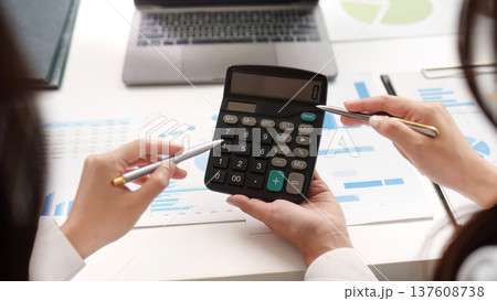 Financial Calculation. Two professionals using a calculator to analyze financial data and reports. 137608738