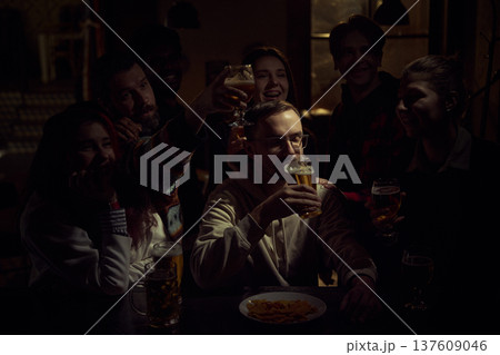 Group of football fans watching game in pub while one man drinks beer calmly during tense match moment 137609046