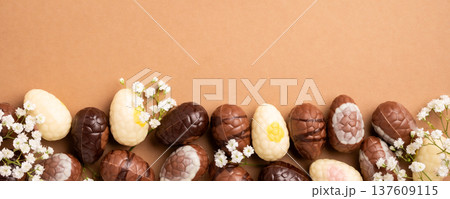 Colorful Easter eggs arranged with delicate white flowers on a brown background for festive decoration Colorful Easter eggs arranged with delicate white flowers on a brown background for festive decoration 137609115