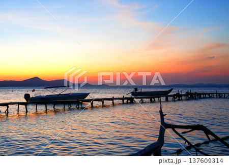 Fishing boats at pier on sunrise. Fishermen's boats at wooden pier in sea. Shore fishing village 137609314