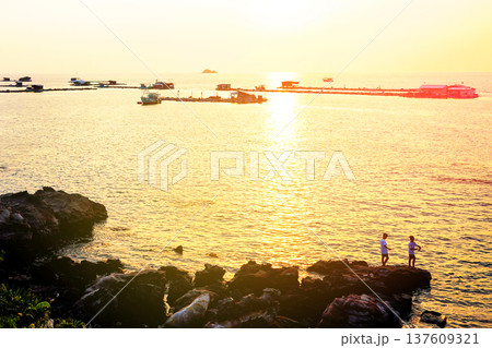 Sunset over water with people standing on rocks near shore in coastal area in Phu Quoc, Vietnam. Sunset over water with people standing on rocks near shore in coastal area in Phu Quoc, Vietnam. 137609321