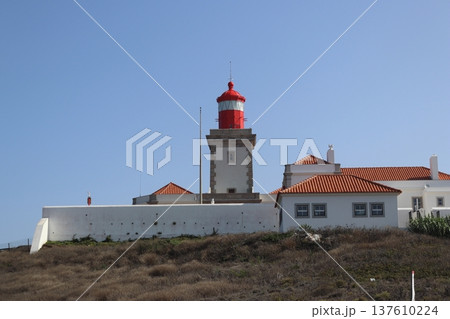 Red lighthouse tower and traditional white buildings at Cabo da Roca, Portugal. 137610224