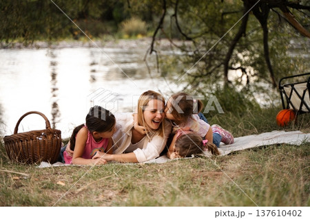 Happy family enjoying a picnic by the river having fun and kissing Happy family enjoying a picnic by the river having fun and kissing 137610402
