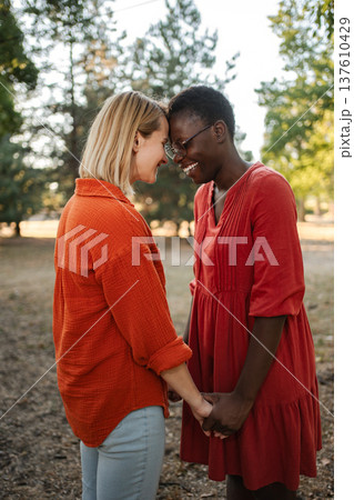 Two Smiling Women Holding Hands and Touching Foreheads in a Park 137610429