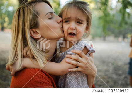Mother comforting her crying daughter at the park Mother comforting her crying daughter at the park 137610430