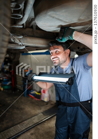 Car mechanic inspecting vehicle undercarriage with work light 137610930