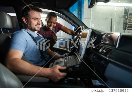 Mechanics performing diagnostics on a car's electronics using a computer 137610932