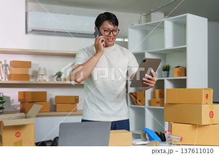 E-commerce. Happy man on phone while managing packages in home office. 137611010