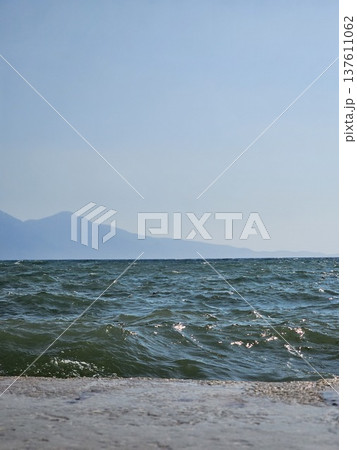 Picturesque view to blue sea and mountain island on horizon in mist. Calm water surface, background for traveling and vacation,Beautiful sea view, sailboats far away in the sea in sunny day. 137611062