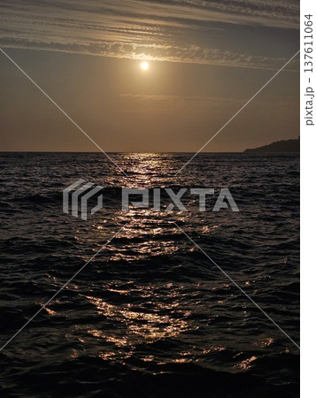 people enjoying sunset at the beach golden sunset illuminates the coastal sea waves and rugged rocks in Kusadasi, Turkey, creating a warm and serene atmosphere against the backdrop of the Aegean Sea 137611064