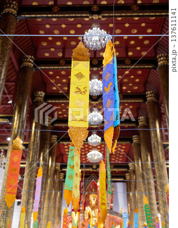 Colorful Thai religious flags hanging inside Buddhist temple. Traditional decorations symbolizing blessings, faith and spiritual harmony in sacred interior setting in Thailand. Colorful Thai religious flags hanging inside Buddhist temple. Traditional decorations symbolizing blessings, faith and spiritual harmony in sacred interior setting in Thailand. 137611141