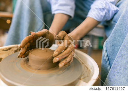 Close up of female hands shaping clay on pottery wheel in ceramic studio, handmade pottery process and traditional craft 137611497