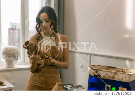 Young female ceramic artist holding handmade clay vase in pottery studio, creative craft process and handmade ceramics production 137611508
