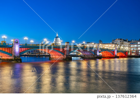 Southwark Bridge spans the Thames River at night in London. City lights reflect on the water, creating a colorful scene. St. Paul's Cathedral is visible in the background. Southwark Bridge spans the Thames River at night in London. City lights reflect on the water, creating a colorful scene. St. Paul's Cathedral is visible in the background. 137612364