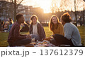 Group of young friends enjoying picnic in sunny city park, casual outdoor gathering with laughter, food and conversation capturing modern lifestyle and social connection 137612379