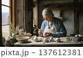 Elderly woman carefully painting Easter eggs at rustic table by window light, traditional spring craft scene showing handmade holiday decoration and family heritage 137612381