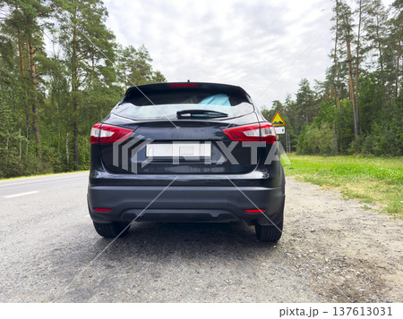 Black car parked on rural road with forest background. Rear view vehicle stands on countryside asphalt. Transport scene for travel, automotive, mobility concept.. 137613031