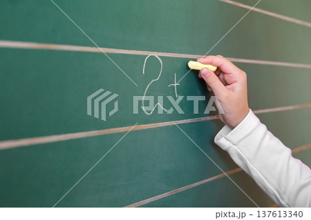 First grade pupil a girl writing on green blackboard at school lesson 137613340