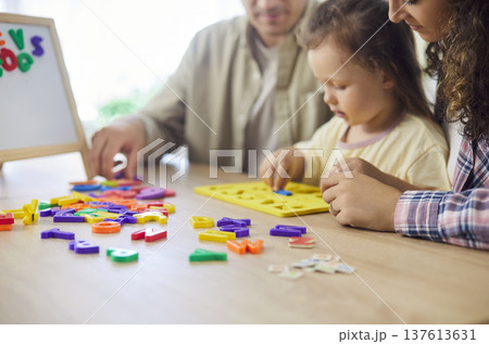 Parents guiding little daughter sorting colorful alphabet pieces during home play Parents guiding little daughter sorting colorful alphabet pieces during home play 137613631