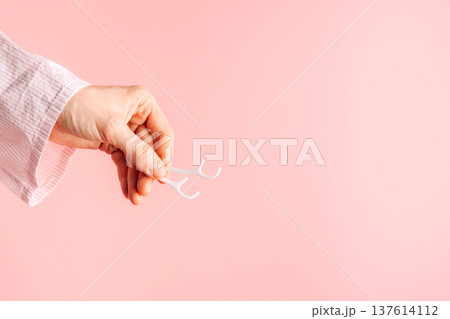 Hand holding a white dental floss pick on pink background, minimal oral hygiene concept with copy space Hand holding a white dental floss pick on pink background, minimal oral hygiene concept with copy space 137614112
