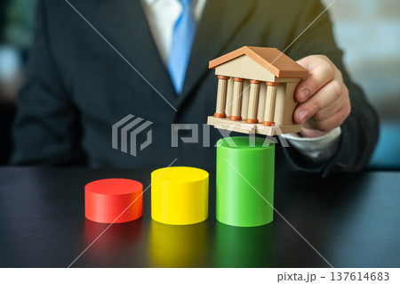 Businessman holds a bank building over a growth chart. Concept of successful business, GDP, income, and positive financial indicators. Income expansion Businessman holds a bank building over a growth chart. Concept of successful business, GDP, income, and positive financial indicators. Income expansion 137614683