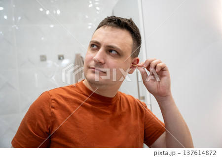 A 35 year old Caucasian man cleans his ears with cotton swabs. Symbolizing personal hygiene 137614872