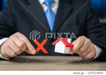 Businessman holding a prohibition sign over a house. Concept of real estate restrictions. 137614897