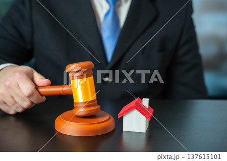Male hand holds a judge gavel near house. Male hand holds a judge gavel near house. 137615101
