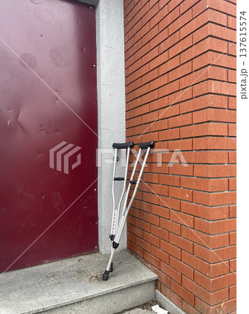 Crutches resting against the wall near a doorway on a cloudy day in a city setting Crutches resting against the wall near a doorway on a cloudy day in a city setting 137615574