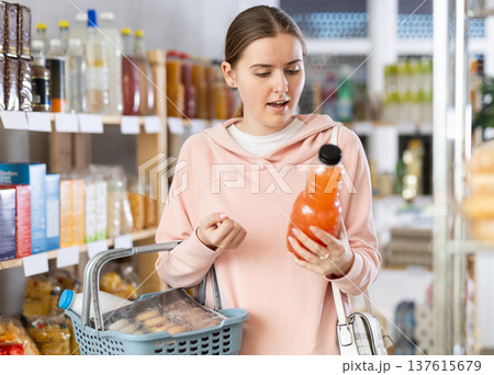 Girl customer in supermarket examines fruit juice, chooses drink in grocery store 137615679