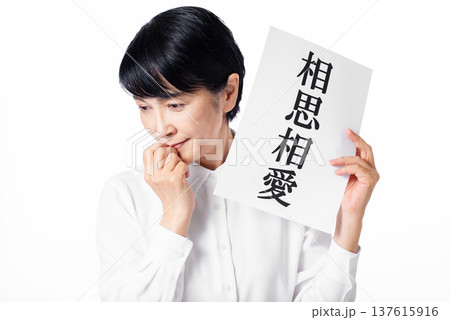 相思相愛と書かれた紙を持ちはにかむ白いシャツを着たシニア女性 137615916