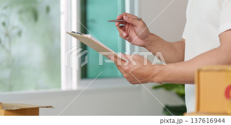 Inventory Management. A man checking stock with a clipboard in a modern workspace. 137616944